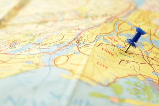 A blue pin pressed into a map detailing the point of interest of New York City in the United States of America.