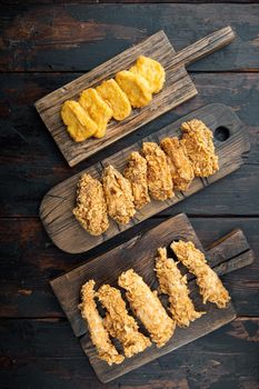 Breaded fried chicken parts on dark wooden background, top view.
