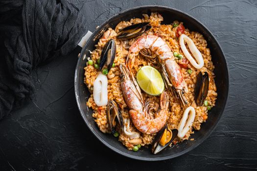Paella traditional spanish dish served in frying pan, on black textured surface, top view, food photo.