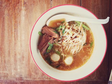 Delicious noodles with pork and pork balls with soup in white in Thai style food. Thai peoples call Boat Noodles, breakfast with bowl on wooden background meat. Noodle of traditional Thai food.