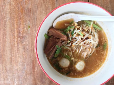 Delicious noodles with pork and pork balls with soup in white in Thai style food. Thai peoples call Boat Noodles, breakfast with bowl on wooden background meat. Noodle of traditional Thai food.