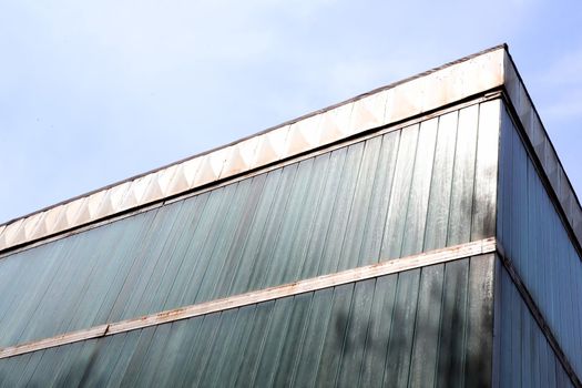 Architectural building on a background of sky. The walls of the building are made of panels. The sun is shining on the building