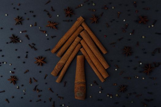 Flat lay with christmas tree made of cinnamon sticks on dark black table decorated with with spices. Winter holidays and cooking concept. High quality photo