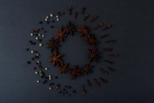 Top view of two circles made of different spices, anise stars, pepper and dry cloves on dark black table. Concept of cooking and baking with spices. 