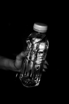 Transparent plastic bottle of water without a label in a woman's hand with long nails. Black and white photo