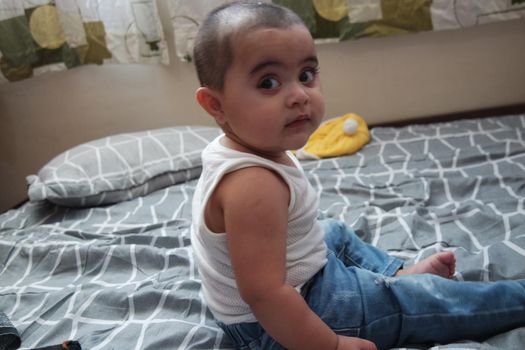 Baby girl with lovely face, big eyes and cute face gesture. Baby girl with jeans playing on bed.