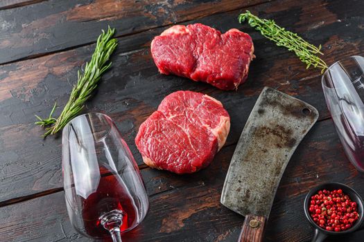 Raw rump steaks with american butcher cleaver and two glass of red wine over dark old wooden background, side view