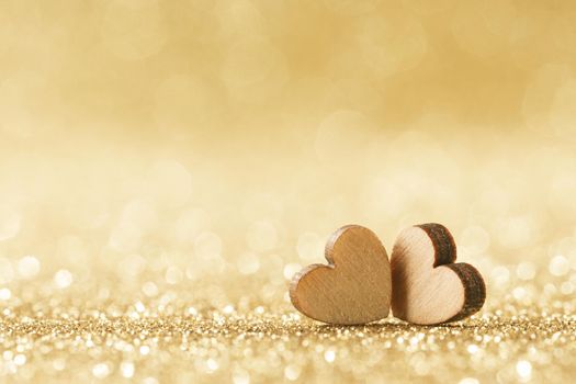 Two small handmade wooden hearts on bright golden lights bokeh background Valentines day card