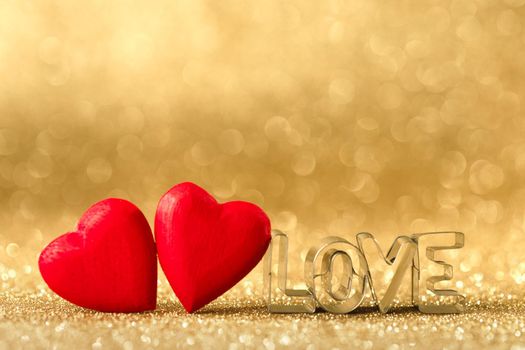 Two red handmade wooden hearts and word love on golden bright glitter lights bokeh background