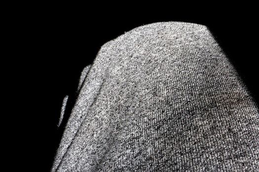 Fabric texture of gray stretch men`s sports pants. Around the fabric is a black background, the fabric is brightly lit by the sun.