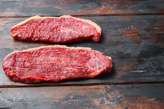 Organic picanha beef meat steaks, over dark old wooden background, side view space for text