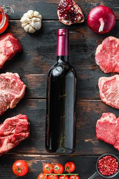 Meat beef steaks frame concept, with different steak cuts and red wine bottle in frame on dark old wooden table top view