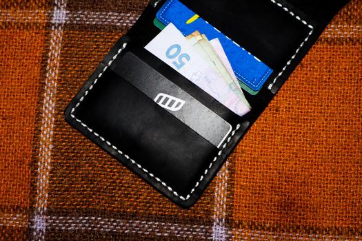 Leather wallet stitched with white threads with cards and money on a plaid in a cage