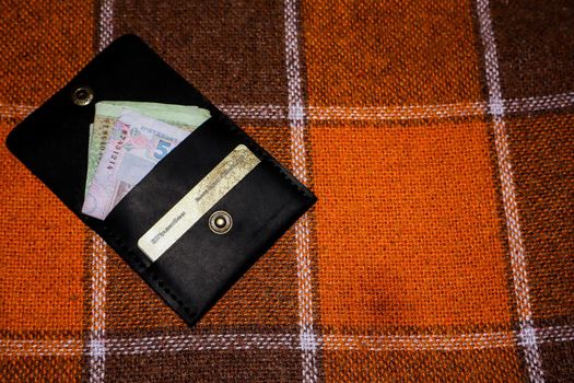 Leather wallet stitched with white threads with cards and money on a plaid in a cage
