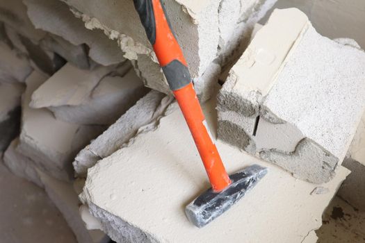 A hammer with a rubberized orange handle stands on construction debris