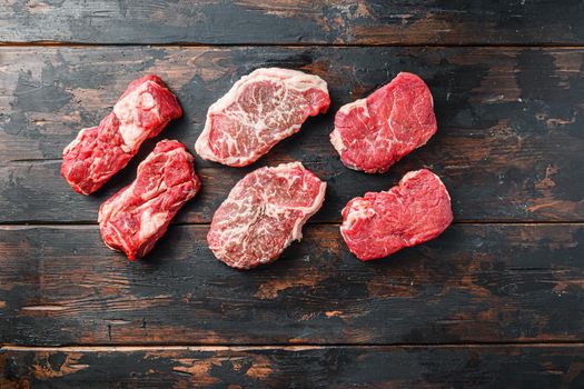 Variety of organic raw beef steakes rump, chuck roll and top blade cut on old rustic dark wooden background, top view with space for text