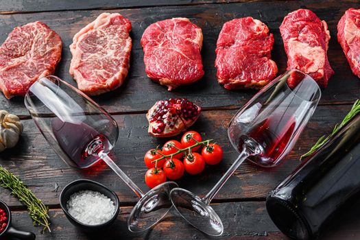 Set of different raw beef steaks with seasonings and red wine in bottle and glass on old wooden dark planks side view