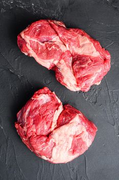 Raw chuck eye roll steak cuts, top view on black textured.
