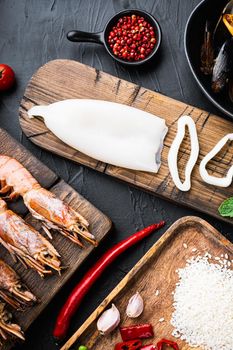 Ingredient for a spanish seafood paella with rice, pea,pepper and shellfish on black textured background, top view, food photo.