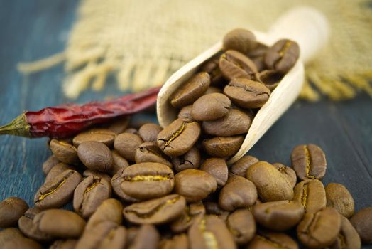 Macro photo of roasted coffee beans spilling from a wooden scoop near dried red chili pepper