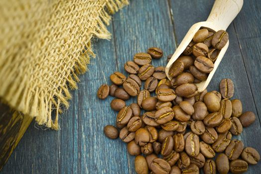 Roasted coffee beans spilling from a wooden scoop on wooden and hessian or burlap fabric background