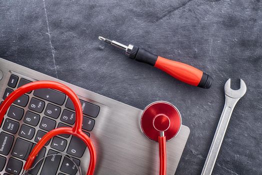 Computer repair or maintenance concept with a stethoscope to check the status or health of the device on top of a laptop with screwdriver and spanner