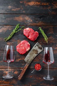 Raw rump steaks with american butcher cleaver and two glass of red wine over dark old wooden background, top view space for text