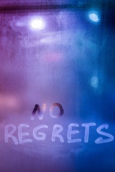 words no regrets hand written on purple-blue night foggy window glass - closeup with selective focus abstract concept