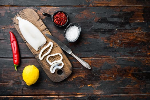 Fresh calamari, sliced on cutting board with spices and lemon on old wooden dark table, top view with space for text, food photo.