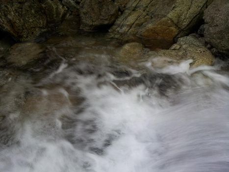 Blurred or unfocused view of flowing water stream in between stones. Flowing water background for texture and advertisements