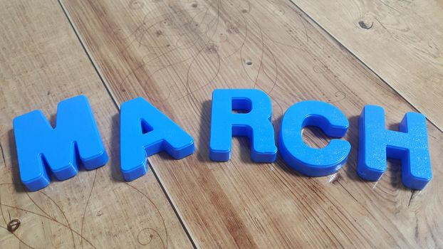 Plastic colored alphabets making words are placed on a wooden floor. These plastic letters can be used for teaching kids.