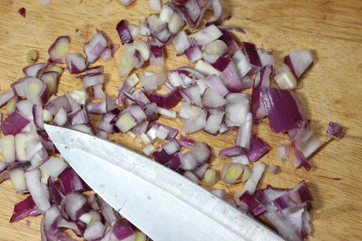 Chopped white onion with sharp knife on wooden cutting board. High angle top view of chopped onions pieces