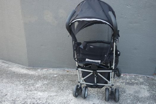 Black color baby stroller with head covering. Stroller is with concrete background