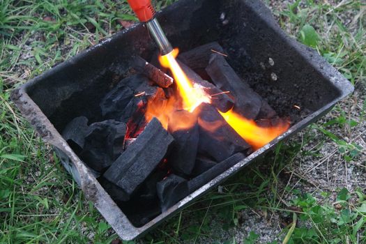 Fire on logs in fire pot with embers and burning coal. Bonfire with blazing red and orange fire flames. Fire background with woods and planks on fire at night view.