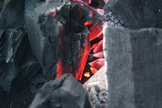 Fire on logs in fire pot with embers and burning coal. Bonfire with blazing red and orange fire flames. Fire background with woods and planks on fire at night view.