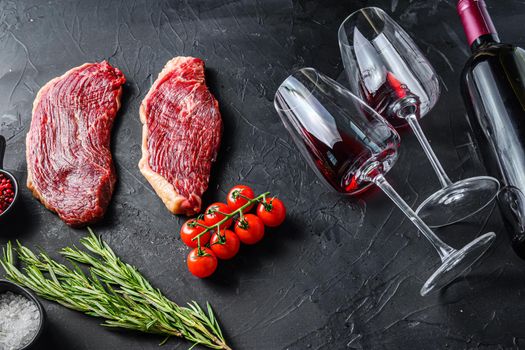 Organic picanha steaks near bottle and glass of red wine, over black textured table side view