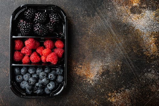 Ripe berries in tray from market, blueberries, raspberry with blackberry, top view with copy space, on old dark table