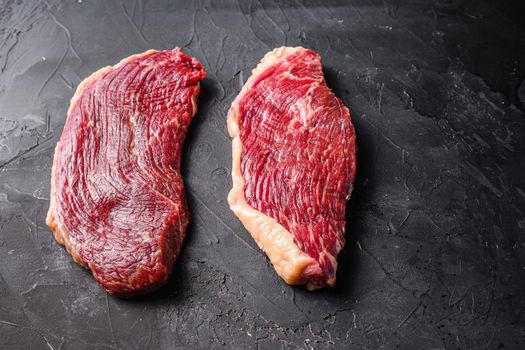 Organic raw picanha beef steaks, on black textured background, side view