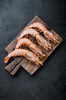 Fine selection of tiger prawns on cutting board on black textured background, top view, food photo.