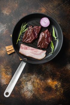Beef liver sliced with bacon on grill pan over rustic background, top view.