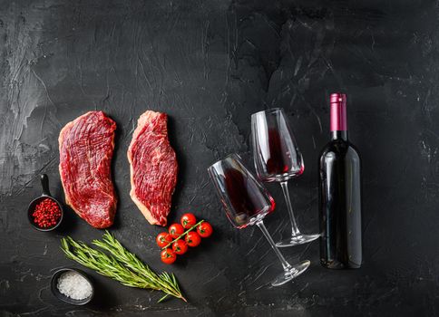 Raw picanha beef cuts with glasses of red wine, flat laym over black background space for text. Big size