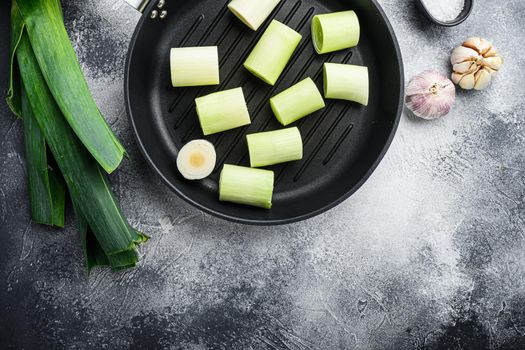 Raw braised Leeks on grill pan uncooked with herbs ingredients , on textured grey background top view with space for text