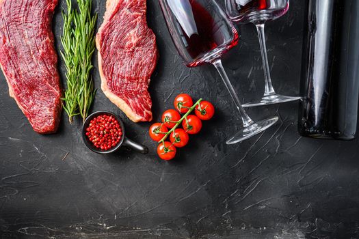 Raw picanha steaks near bottle and glass of red wine, over black textured table top view with space for text
