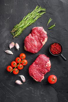 Raw rump steaks from organic beef meat cuts with rosemary, garlic and spices over black textured background, top view