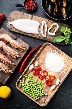 Fresh uncooked paella ingredients with king prawns, mussels and squid on black textured background, top view, food photo.