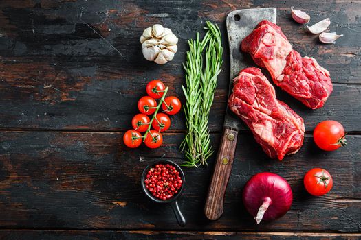 Organic raw chuck eye roll beef steak over old butcher cleaver with rosemary red onin, garlic peppercorns and tomatoes on old dark wooden table. Top view with space for text