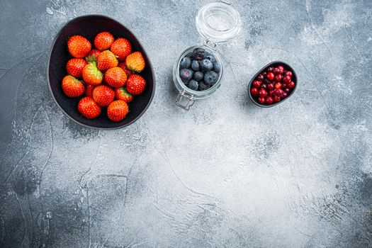 Ripe strawberry, cranberry and blueberry in bowl and jar, flat lay with space for text, on textured background.