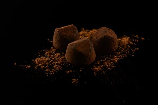 A group of three fine quality chocolate truffles over a black background.