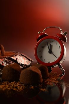 A closeup of a clock in a scene of fine chocolate truffles.