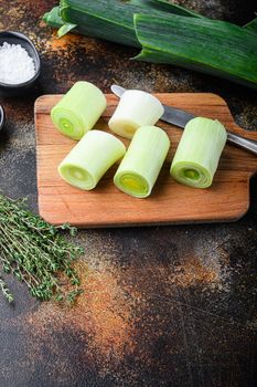 Chopped fresh leek for cooking Braised Leeks on wooden board with herbs ingredients , on rustic metall background dark, side view with space for text